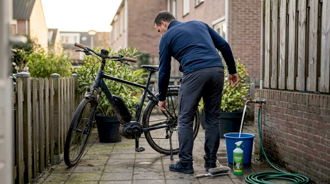 In een groene stadstuin poetst een man zijn e-bike grondig schoon met een borstel.